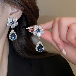 Detailed shot of flower shaped earrings with blue and white zircons on a model