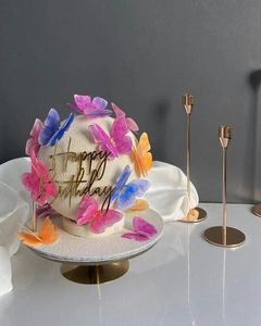 Macro shot of elegant birthday cake with colorful butterflies and golden Happy Birthday topper
