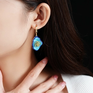 Close-up of vintage gold hoop earring with blue enamel flower charm on model
