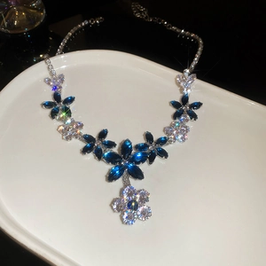 Close-up of floral necklace with blue and clear zircons on a white plate