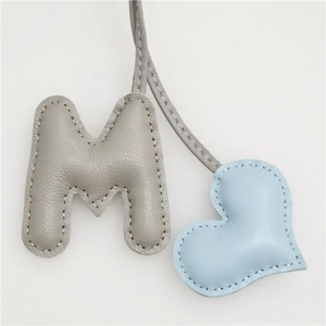 Detailed view of handmade leather letter M and heart charm with refined stitching
