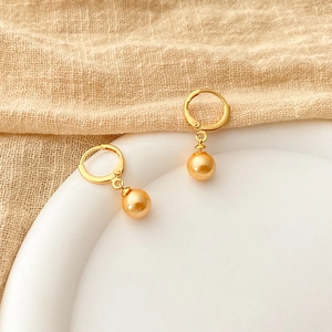 Close-up of 18K gold plated hoop earrings with iridescent pearl drops on a beige linen