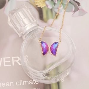 Golden butterfly necklace with purple and blue gradient crystal pendant on perfume bottle