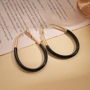 Minimalist gold and black enamel oval hoop earrings on a vintage paper background
