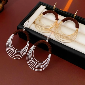 Close-up of gold and silver multilayer oval earrings with brown fabric wrapped details
