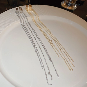 Detailed view of silver and gold C-shaped chain tassel ear cuffs on white ceramic plate