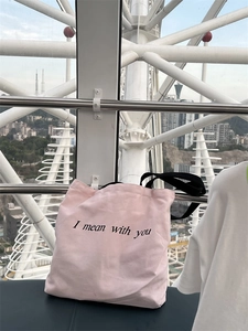 Close-up of pink canvas tote bag with black handle and 'I mean with you' print