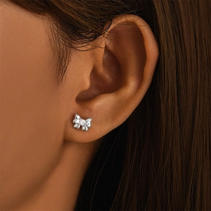 Close-up of a silver bow earring with a clear gemstone on a model's ear cartilage