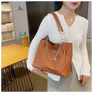 Detail view of a large brown tote bag featuring textured leather and a silver chain strap