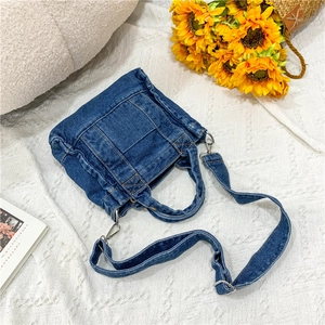 Detail of blue denim mini tote bag with adjustable strap on white textured fabric