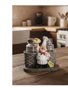 Detail of two glass spice shakers with a resin chef figurine on a textured wood tray