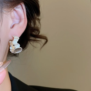 Detail showing irregular white textured C-shaped hoop earrings on a female model