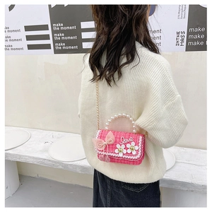 Pink tweed crossbody bag for kids with pearl handle and bow, worn by a child model