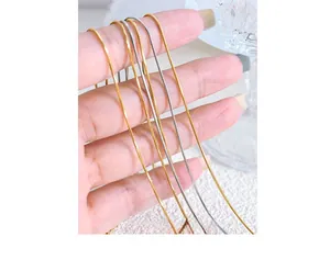 Close-up of thin 18K gold and silver snake bone chains held to show fine texture