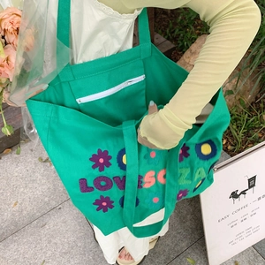 Detail of green canvas tote bag featuring floral embroidery and white inner zipper pocket