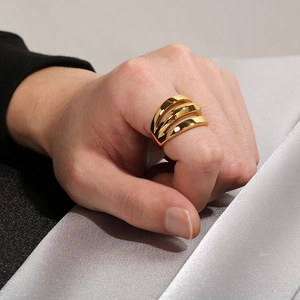 Detail of a three-layered wavy golden ring shown on a finger with a luxury silk background