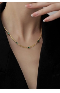 Vista dettagliata di una collana a serpente dorata con cinque zirconi verde smeraldo sulla clavicola
