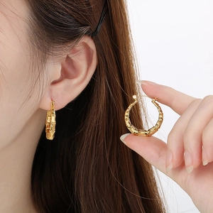 Detail of gold U-shaped bamboo texture earrings worn by model on white background