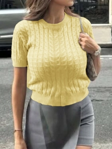 Détail d'un pull en tricot torsadé jaune à manches courtes montrant la texture du tissu