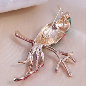 Back view of a gold magpie brooch with red and green enamel details on a pin base