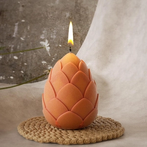 Detailed close-up of a lit orange 3D dragon egg silicone candle mold on a woven mat