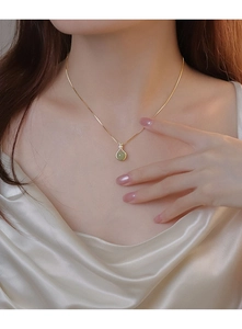 Gros plan d'un collier avec pendentif poire verte porté sur un tissu en soie élégant