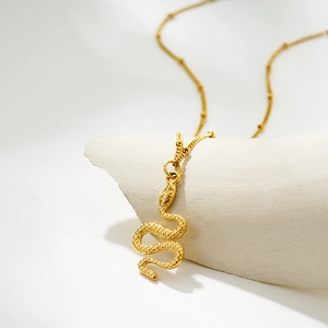 Detailed close-up of golden snake pendant with intricate scale textures on a stone pedestal