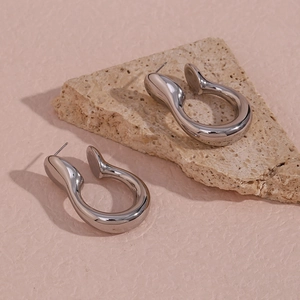 Macro shot of silver U-shaped hollow hoop earrings on textured natural stone