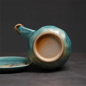 Detail of teal glazed ceramic pot with hemp rope handle and matching saucer on grey surface