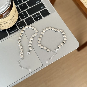 Minimalist silver heart link bracelet and necklace set on a sleek metallic laptop surface