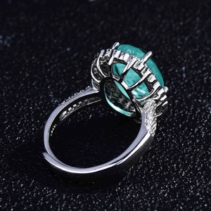 Macro detail of oval green gemstone ring with pavé diamonds on a black textured background