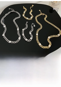 Flat lay of gold and silver curb chains with rhinestone heart pendants on black background