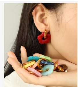 Macro shot of colorful resin flower earrings with golden hoops on a hand