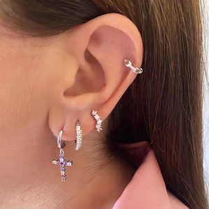 Detail view of silver cross earrings set with colorful cubic zirconia on ear lobe