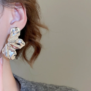Macro detail of silver-tone crinkled texture earrings with liquid metal aesthetic on model