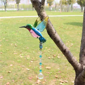 Detail of hummingbird suncatcher with colorful wings and faceted crystal ball on tree branch