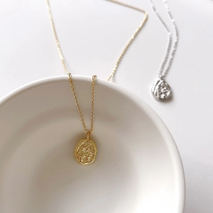 Detail of irregular textured oval pendants in gold and silver finish with minimalist chains
