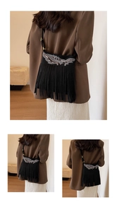 Detail of black suede crossbody bag with fringe tassels and silver wing embroidery