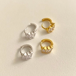 Detail of silver and gold huggie earrings with step-cut cubic zirconia on beige background