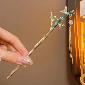 Detailed shot of bamboo-style gold hair stick with green enamel, tassel and butterfly