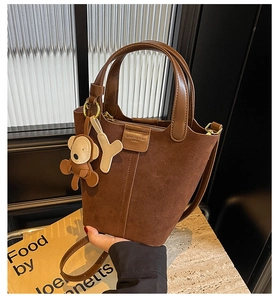 Detailansicht einer braunen Eimertasche mit Lederriemen und Affen-Anhänger