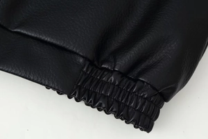 Detailed close-up of black leather jacket showing elastic cuffs and premium grainy texture
