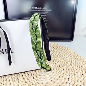 Macro detail of a green braided headband with rhinestones on a woven rustic texture