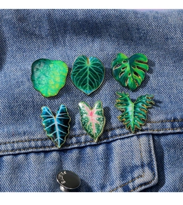 Close-up of tropical leaf enamel pins and badges on blue denim jacket pocket