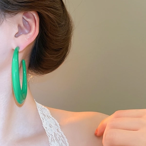 Detailed close-up of a large glossy green C-shape resin hoop earring on a model