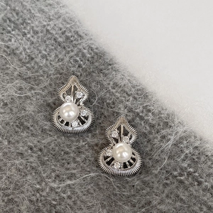 Detail of silver drop earrings with a central pearl and zircon accents on grey knit