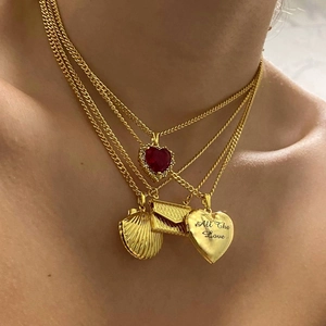 Detail van gelaagde gouden ketting met schelp en hart hanger gegraveerd met All the Love