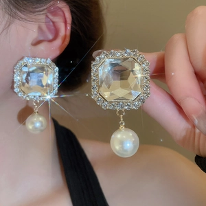 Close-up of vintage gold drop earring with square zircon and white pearl dangle