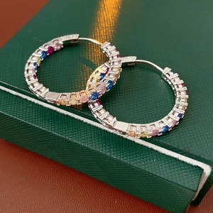 Dettaglio di orecchini a cerchio in argento con zirconi colorati su scatola verde