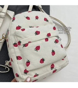 Detail of white corduroy backpack featuring red strawberry prints and zipper pocket